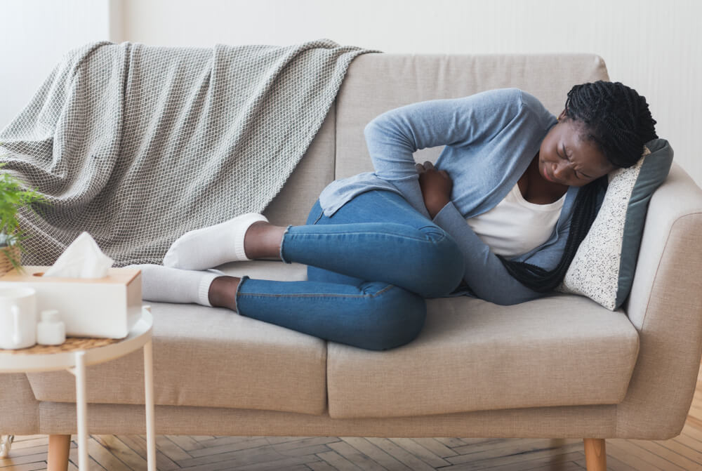 Menstrual Pain. Sick Young Black Woman Lying On Couch At Home Suffering From Abdominal Ache