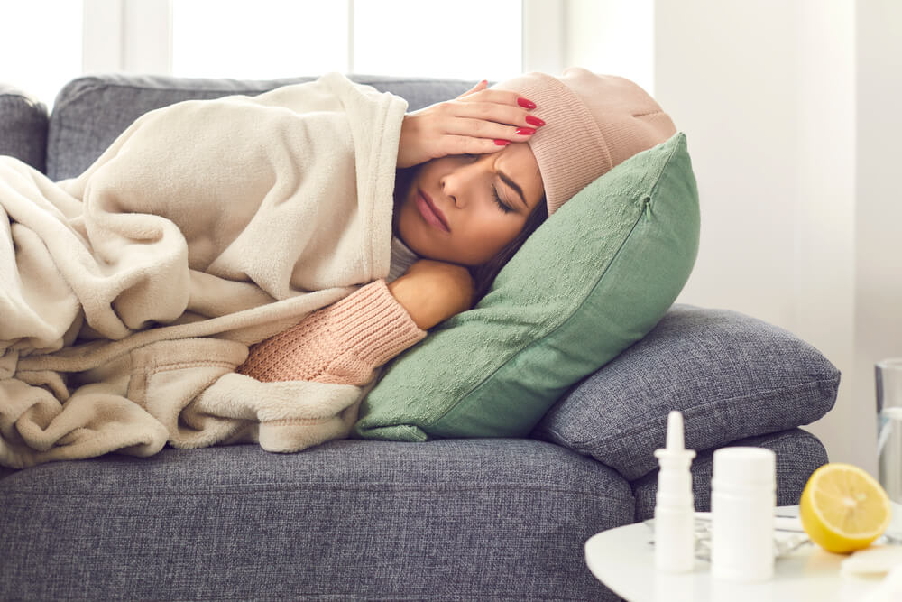 Close Up of a Sick Woman With Flu, Fever and Headache Lying Wrapped in a Plaid on the Couch.