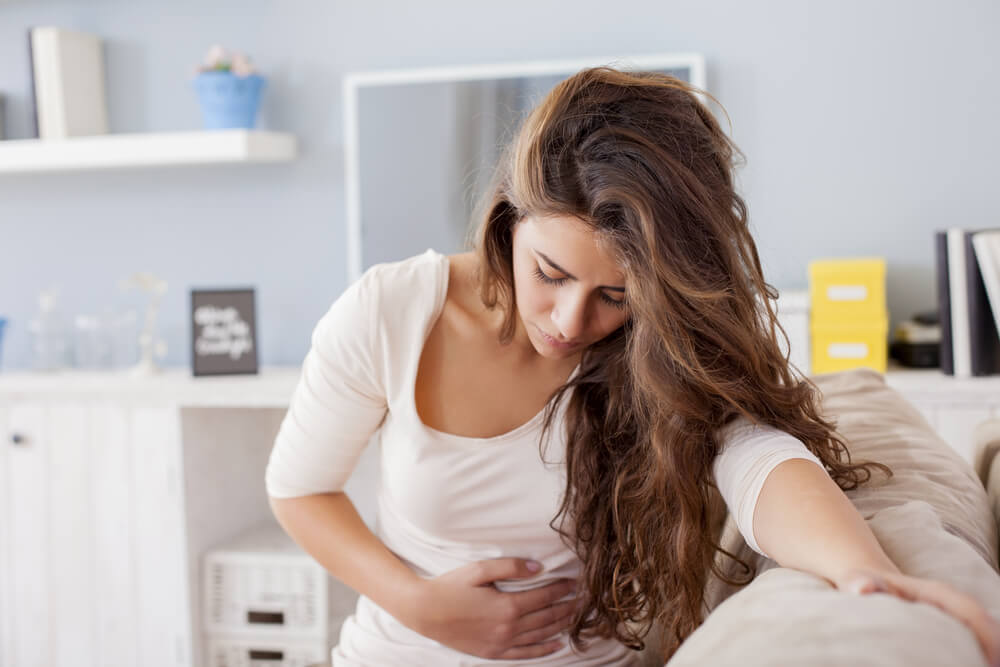 Young Woman Sitting on the Bed With Hard Stomach Pain