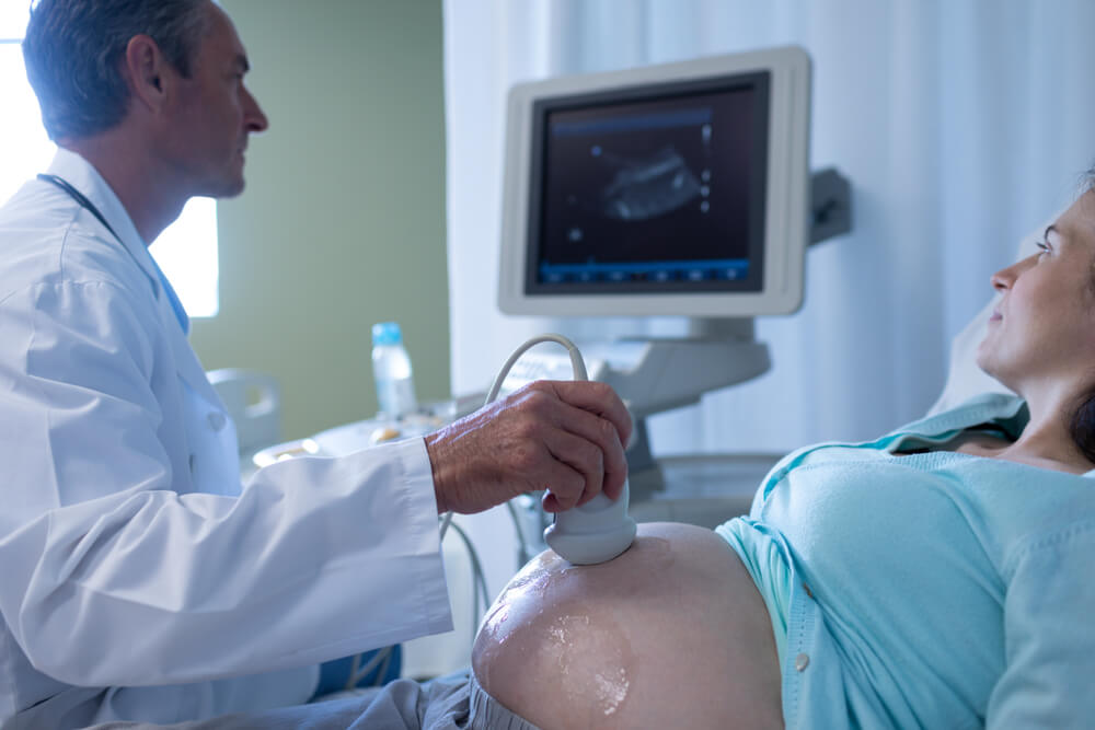 Side View of Caucasian Male Doctor Doing Ultrasound Scan for Pregnant Woman in Hospital