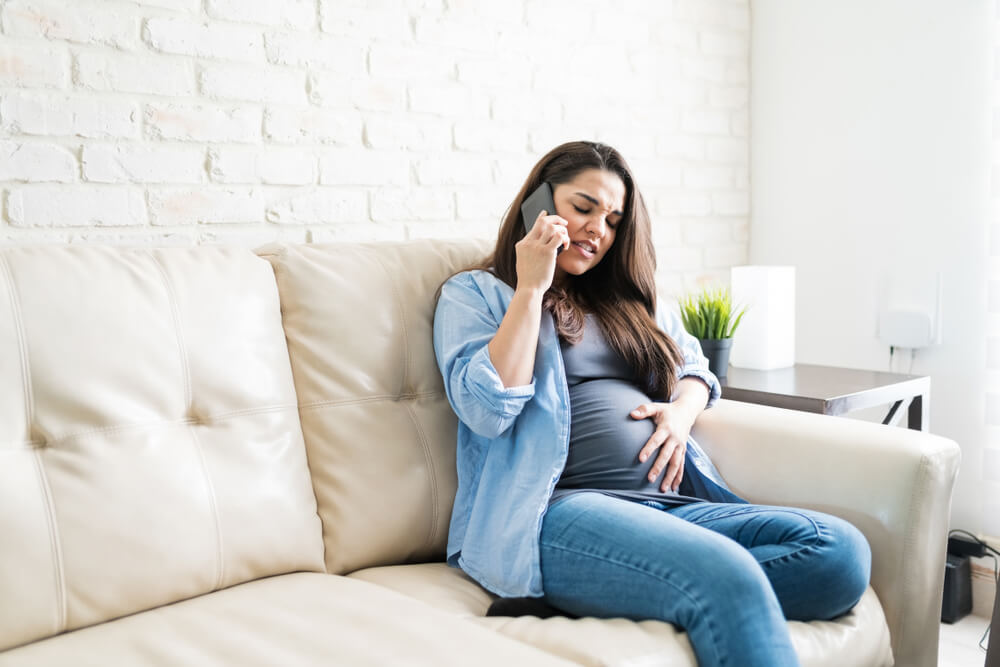 Pretty Pregnant Woman Talking on Mobile Phone While Touching Her Baby Bump During Pain at Home