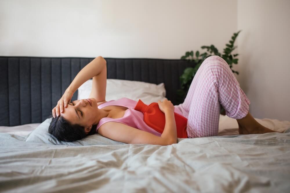 Menstrual cramps, woman warming lower abdomen with a hot water bottle.