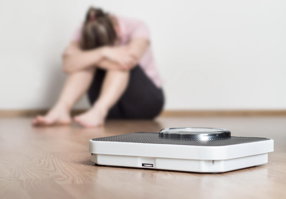 Scale and Depressed, Frustrated and Sad Woman Sitting on Floor Holding Head and Arms on Knees.