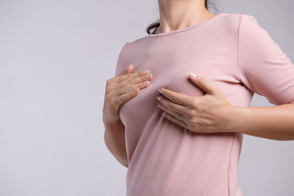 Woman Hand Checking Lumps on Her Breast for Signs of Breast Cancer on Gray Background.