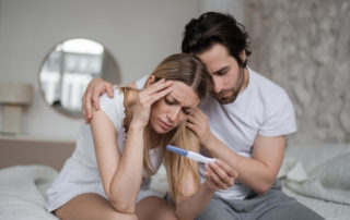 Upset Young Husband Comforting His Depressed Young Wife With Negative Pregnancy Test on Bed at Home.