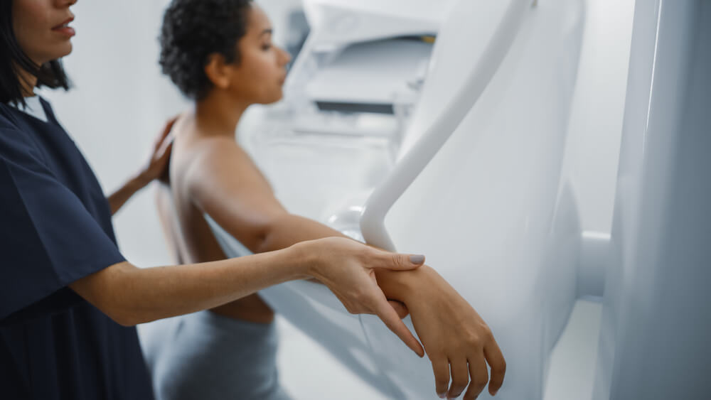 Friendly Female Doctor Explains the Mammogram Procedure to a Topless Latin Female Patient with Curly Hair Undergoing Mammography Scan
