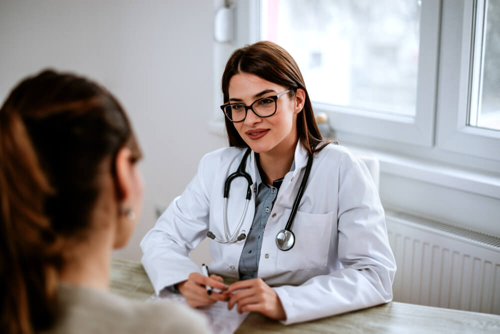 A Woman Sitting at a Table Talking to a Doctor.