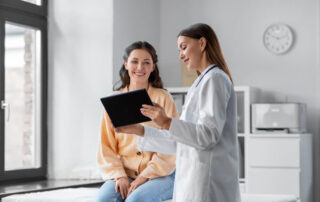 Medicine, Healthcare and People Concept - Female Doctor With Tablet PC Computer Talking To Smiling Woman Patient at Hospital