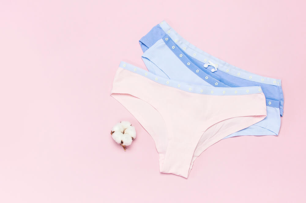 Female pastel cotton set panties and cotton flower on pink background top view flat lay with copy space for text