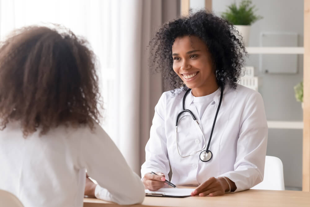 Smiling Female Doctor Talking To Teen Patient Making Notes in Clipboard