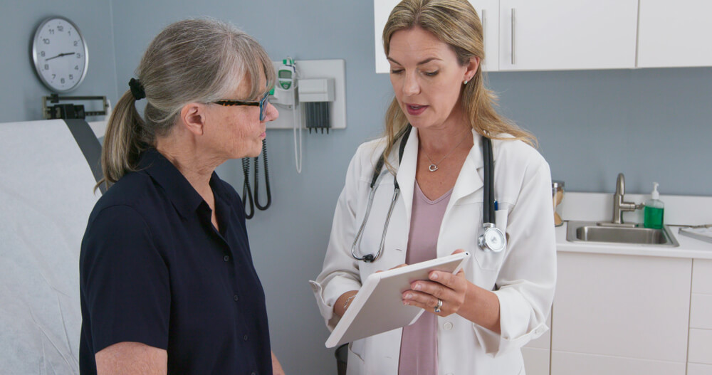 Female Doctor Showing Test Results on Tablet Computer to Caucasian Senior Patient.