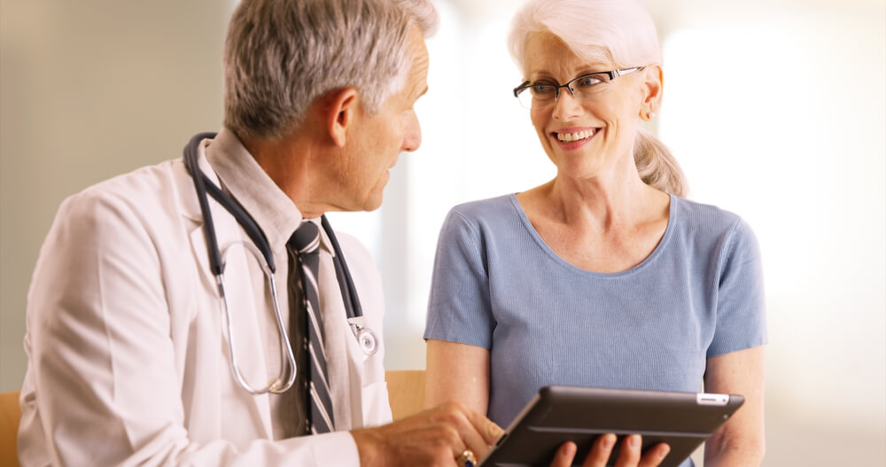 Doctor Going Over Elderly Woman’s Health File in the Office With Tablet