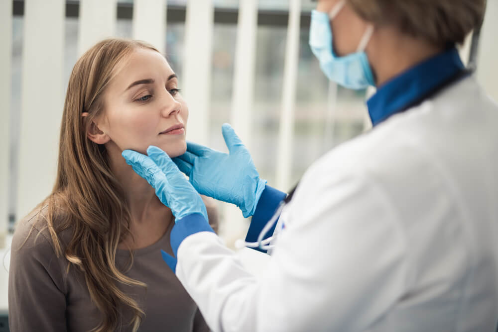 Doctor Woman Examining Tonsils of Smiling Young Lady in Medical Office