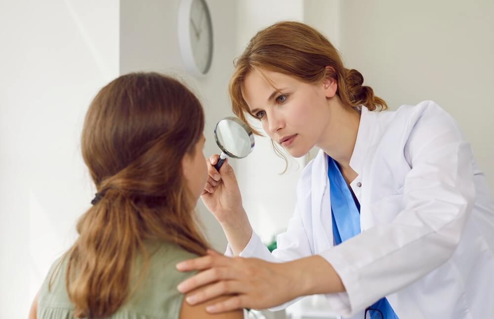 Professional Dermatologist Examines Face of Teenage Girl With Magnifying Glass in Her Office.