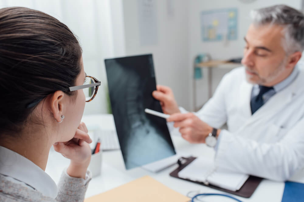 Professional Doctor and Radiologist Giving a Consultation to His Patient, He Is Examining and X-Ray Image and Pointing