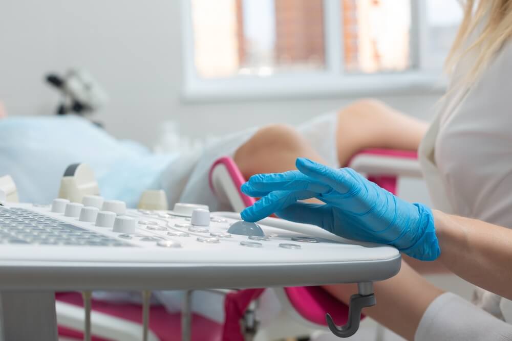 A gynecologist performs an ultrasound diagnostic procedure for a girl lying in a gynecological chair.