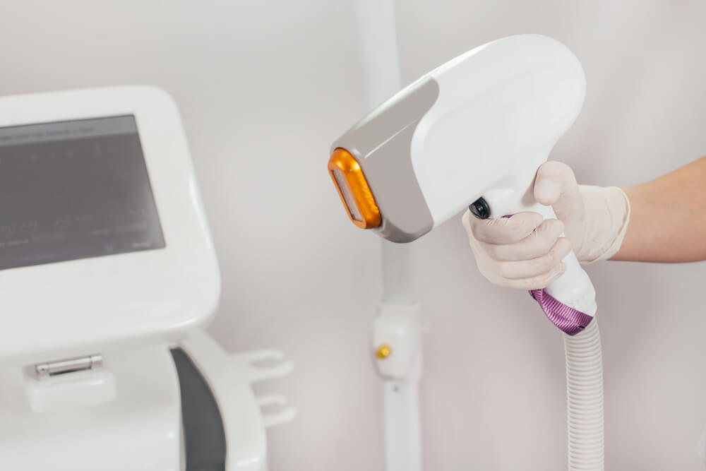 A Woman Tunes a Laser Hair Removal Machine. She Holds a Working Part of the Epilator in Her Hands.