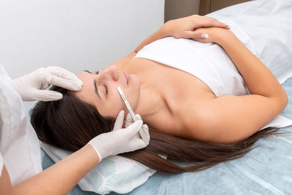 Young Woman in a Beauty Center Performing a Beauty Treatment for the Skin of the Face With the Dermaplaning Technique