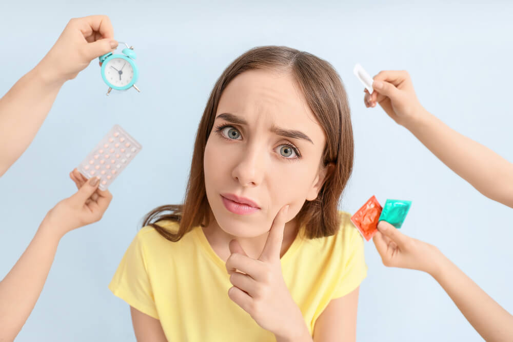 Thoughtful Young Woman and Hands With Different Means of Contraception on Color Background