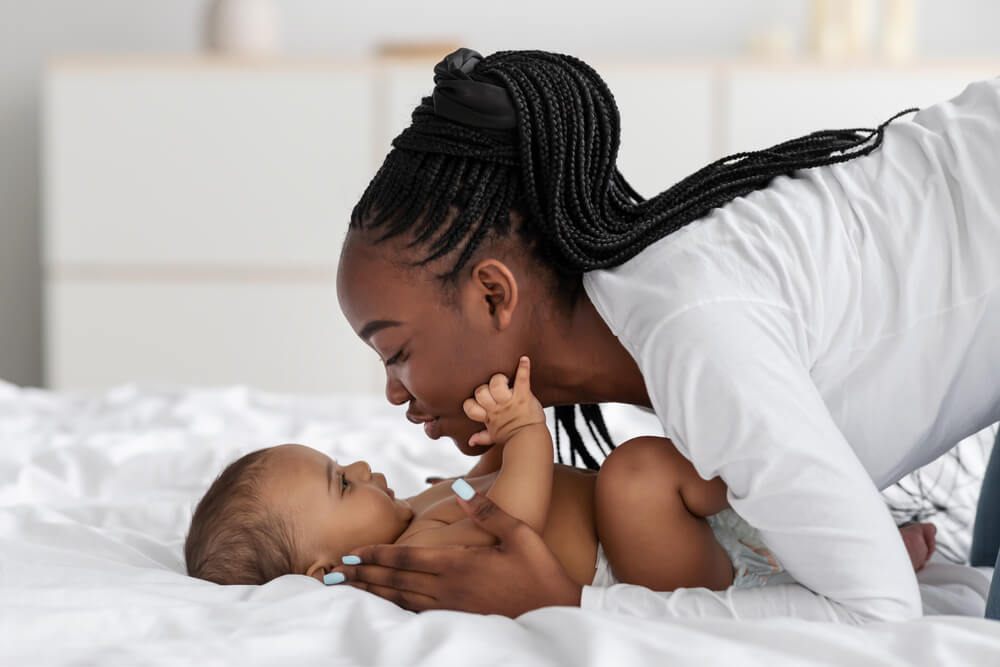 A young mom playing in bed with her infant, kissing baby