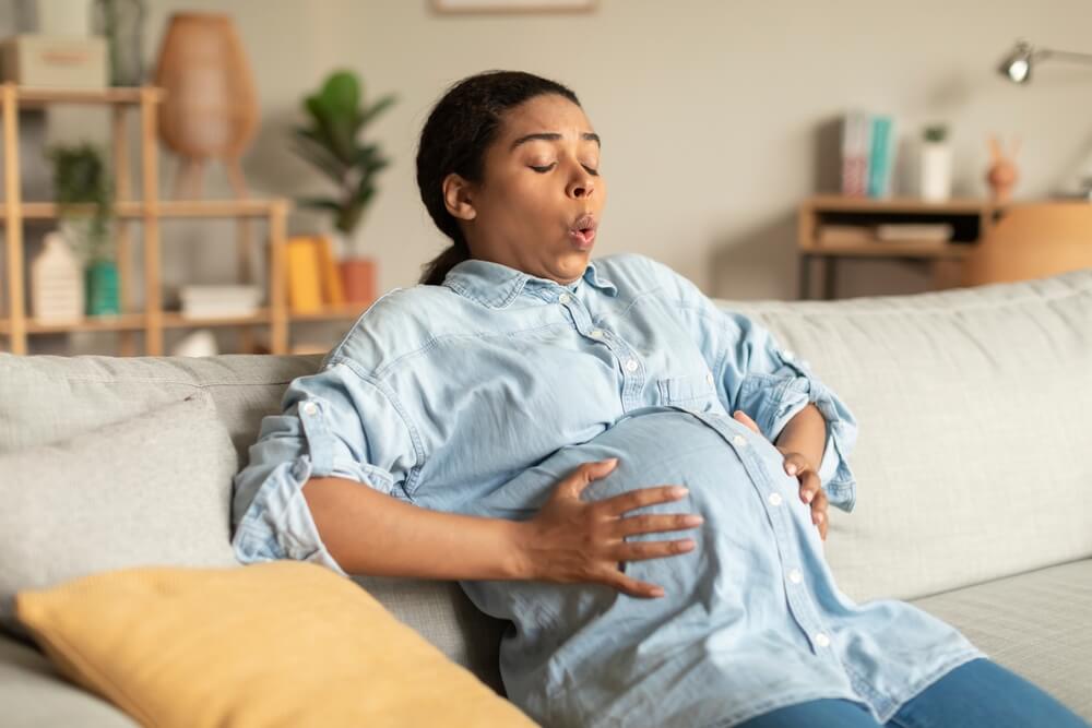 Pregnant Woman Touching Belly While Sitting on Couch at Home