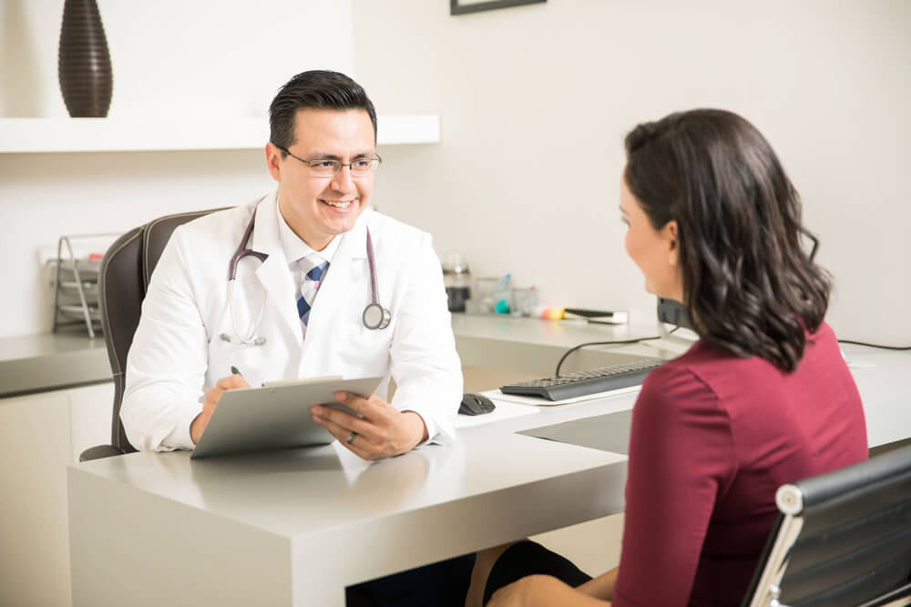 Doctor Taking Some Notes and Talking to a Patient During a Consultation at His Office