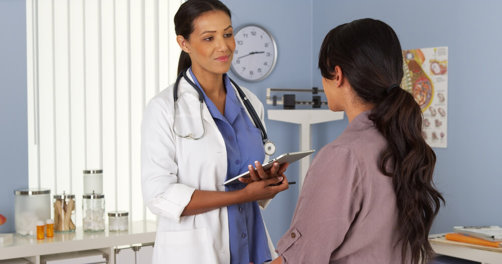 African American Gynecologist Talking To Patient With Tablet