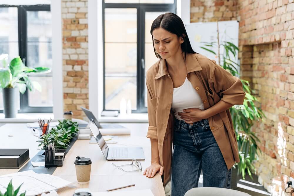 Bad Period. Full Length View Of The Caucasian Woman Suffering With Menstrual Stomach Ache Or Feeling Hurting Stomach In Her Office