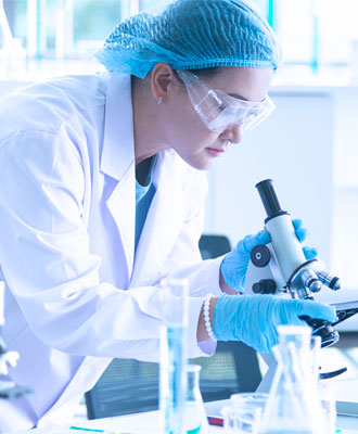 Side-image Doctor Wearing Protective Gloves and Glasses Holding and Looking Through a Microscope