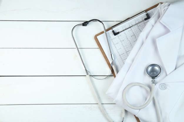 Folded White Coat, Clipboard and Stethoscope on a White Wooden Table