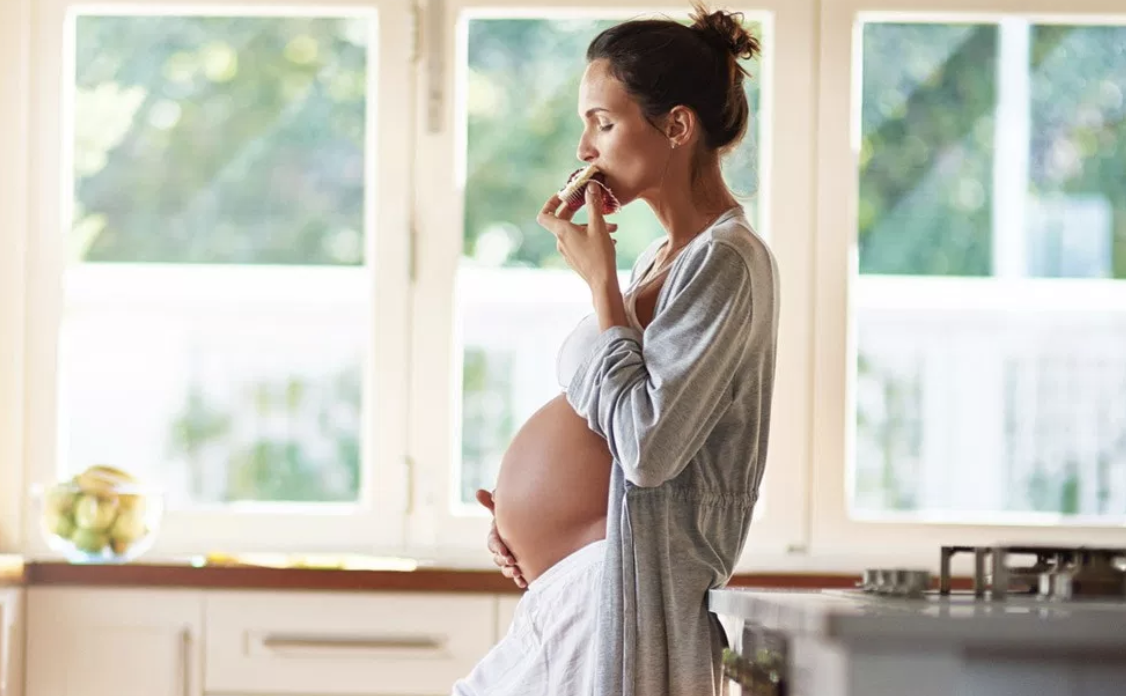 Pregnant Woman Eating a Cupcake in the Kitchen