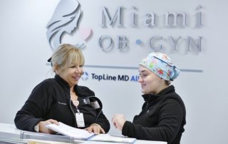 Two Female Employees in Black Standing at the Reception Desk at Clinic