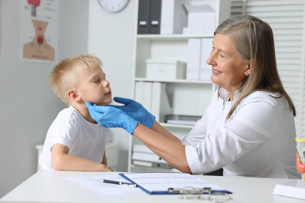 Endocrinologist Examining Boy’s Thyroid Gland at Table in Hospital