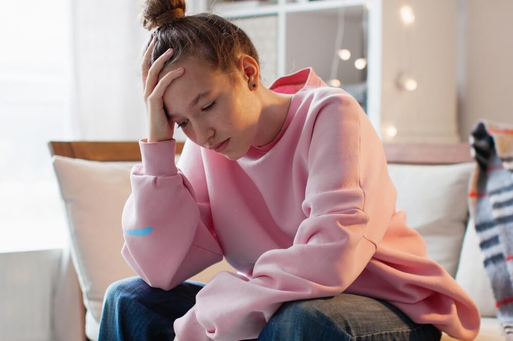 Unhappy Depressed Teenage Girl Sit On Couch at Home Suffer From School Bullying or Discrimination