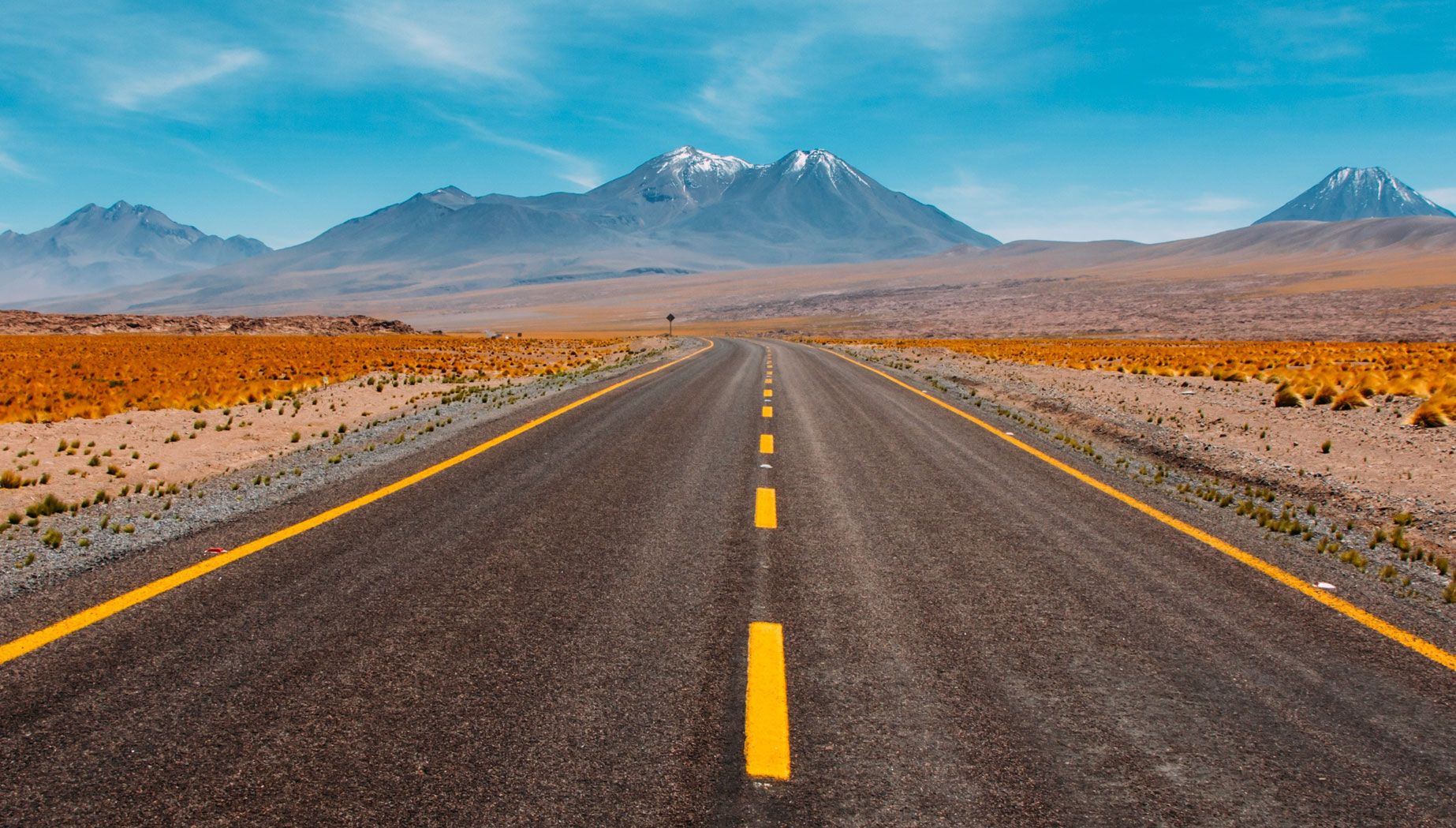 Asphalt Road Through a Desert With Mountain Tops in the Back