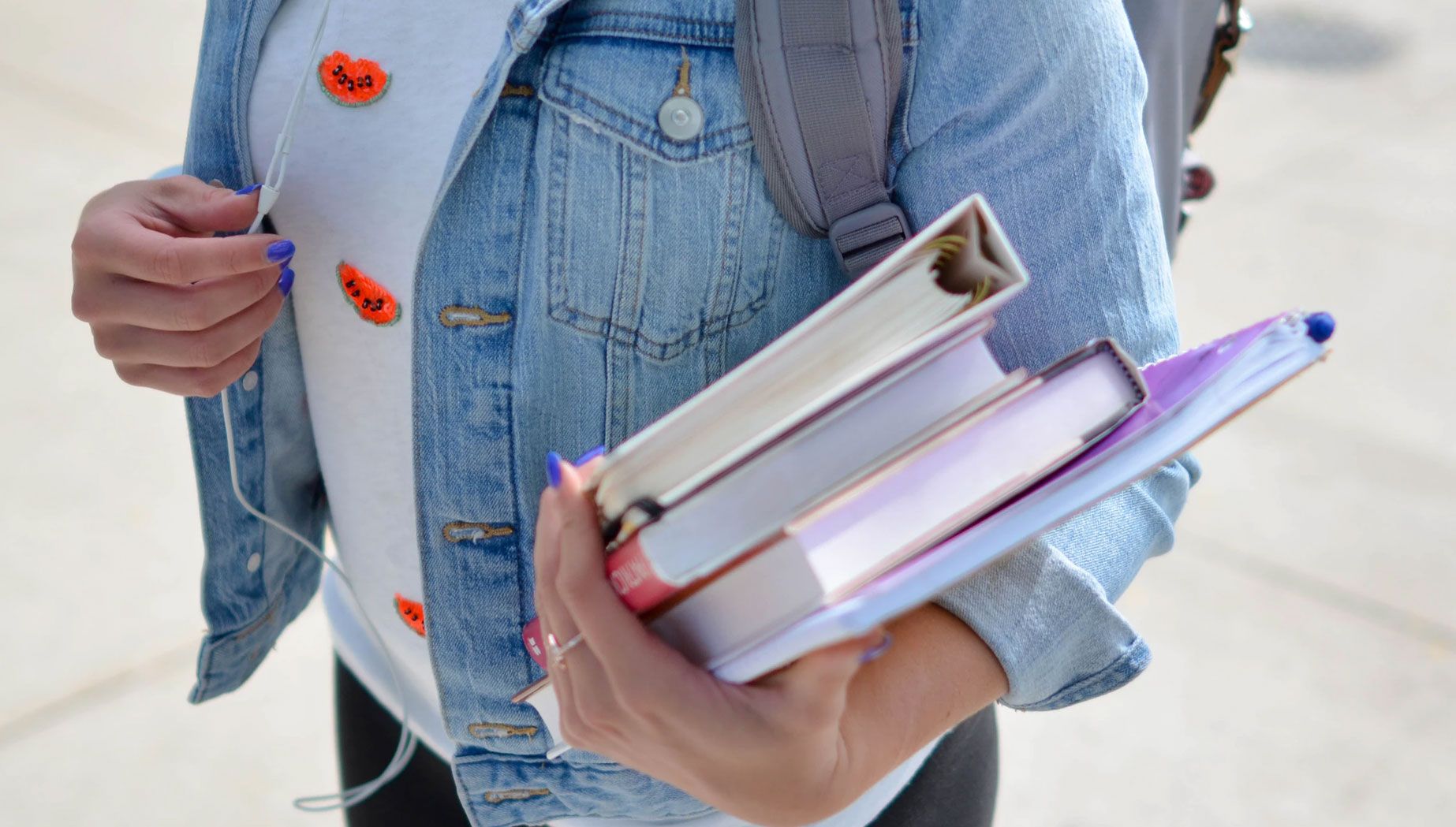 Woman in Blue Jacket and a Backpack Holding Several Books