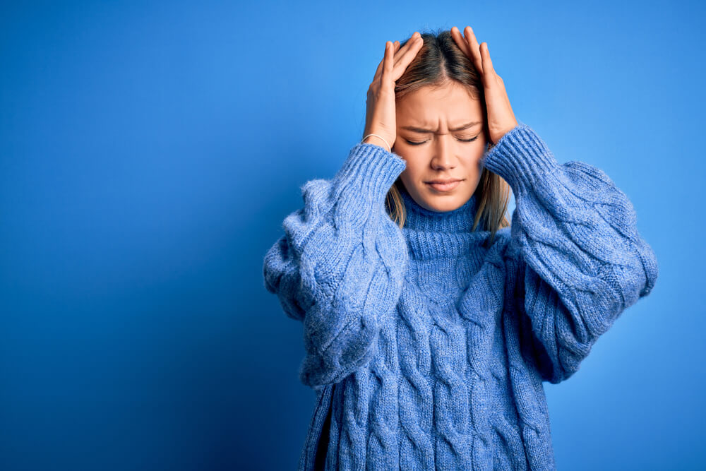 Young Beautiful Blonde Woman Wearing Winter Wool Sweater Over Blue Isolated Background Suffering From Headache Desperate and Stressed Because Pain and Migraine. 