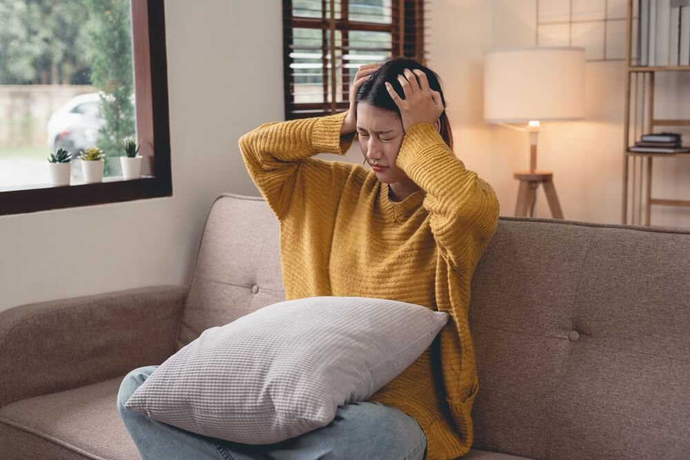 Young Woman Suffering From Headache Sits Alone on the Sofa at Home