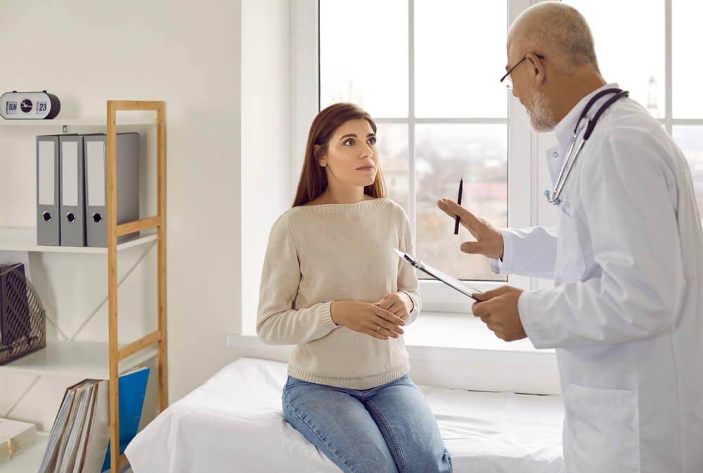 Experienced Senior Doctor at Modern Clinic Talking To Nervous Female Patient.