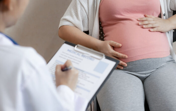 Doctor Writing on Paper, While Talking to Pregnant Woman.