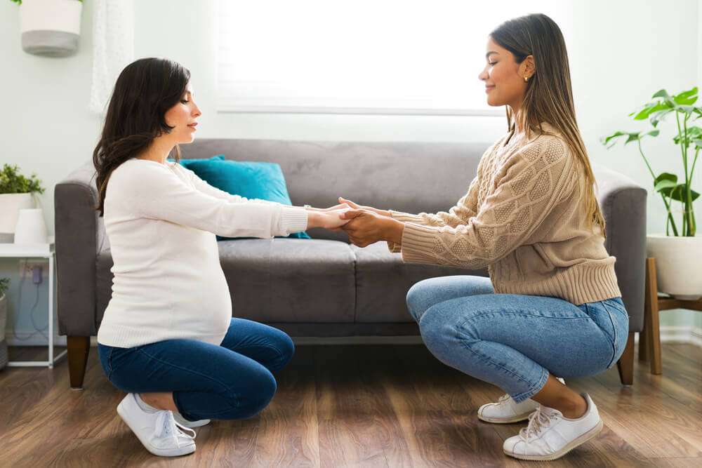 Smiling midwife helping a beautiful pregnant woman with her stretching exercises