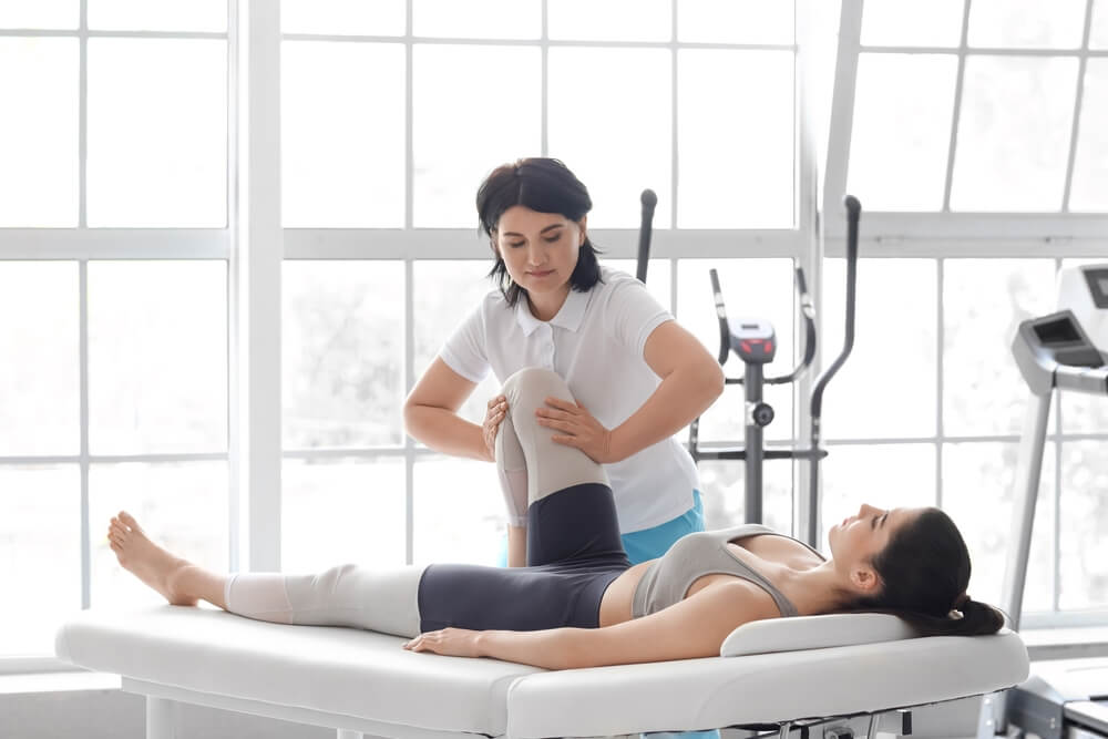 Female Physiotherapist Working With Young Woman on Couch in Rehabilitation Center