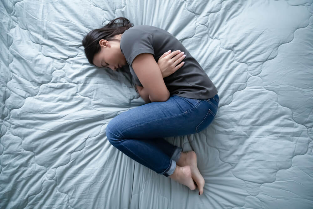 Top View of Unhappy Depressed Young Woman Lying on Bed Suffer From Abortion or Miscarriage