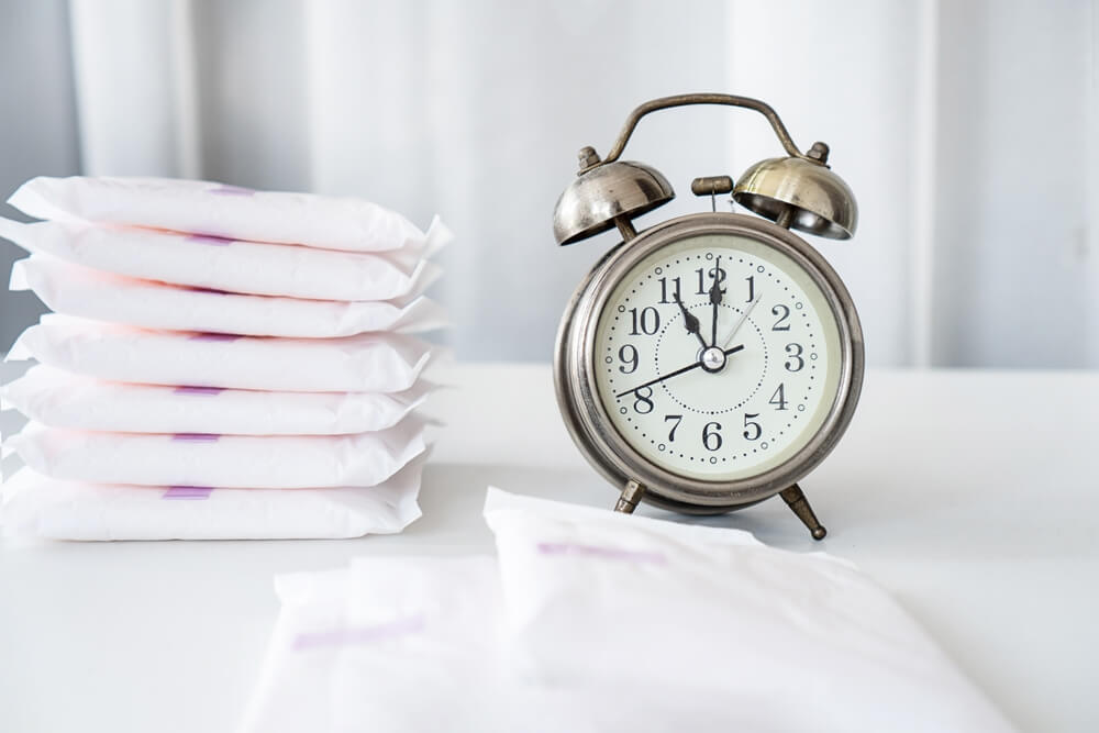 Concept With an Alarm Clock and Menstrual Pads on the Table