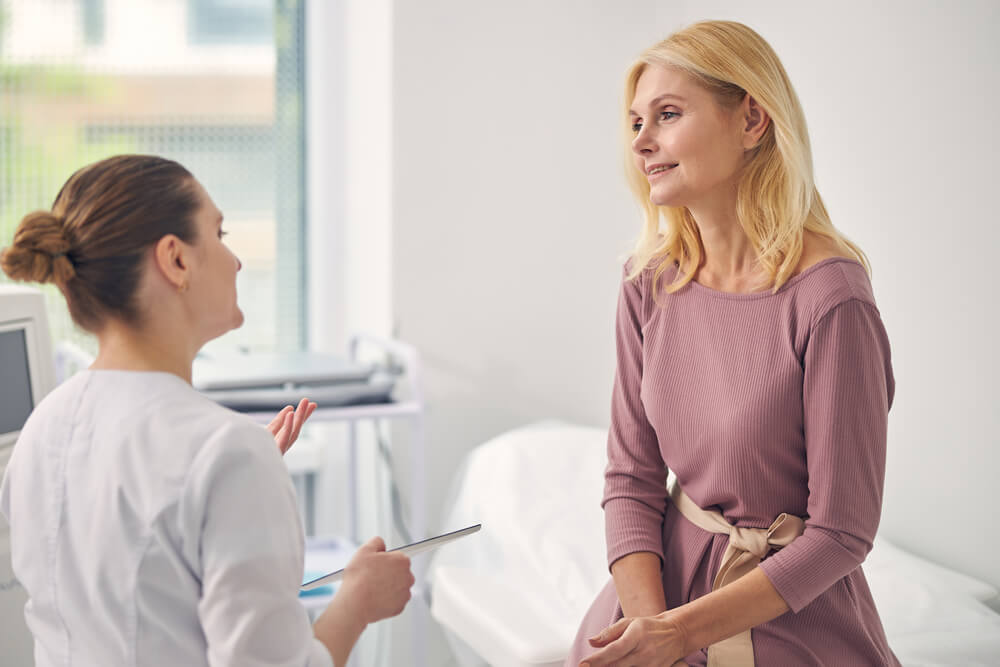 Kind-Mature-Woman-Sitting-Opposite-Her-Practitioner-While-Doing-Health-Checkup