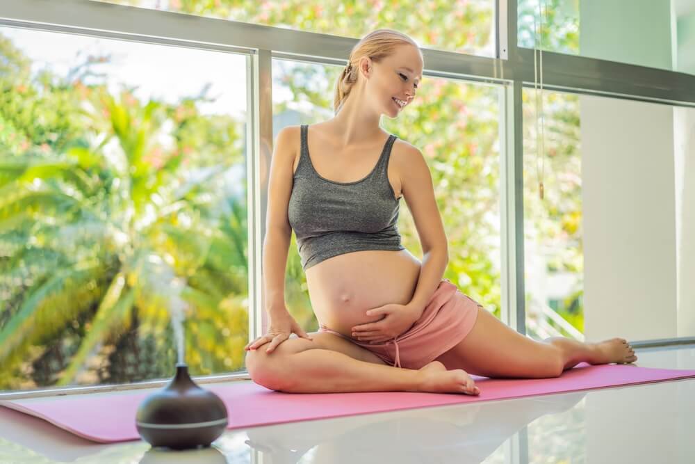 Young Pregnant Woman Doing Yoga Exercises and Meditating at Home With an Aroma Diffuser