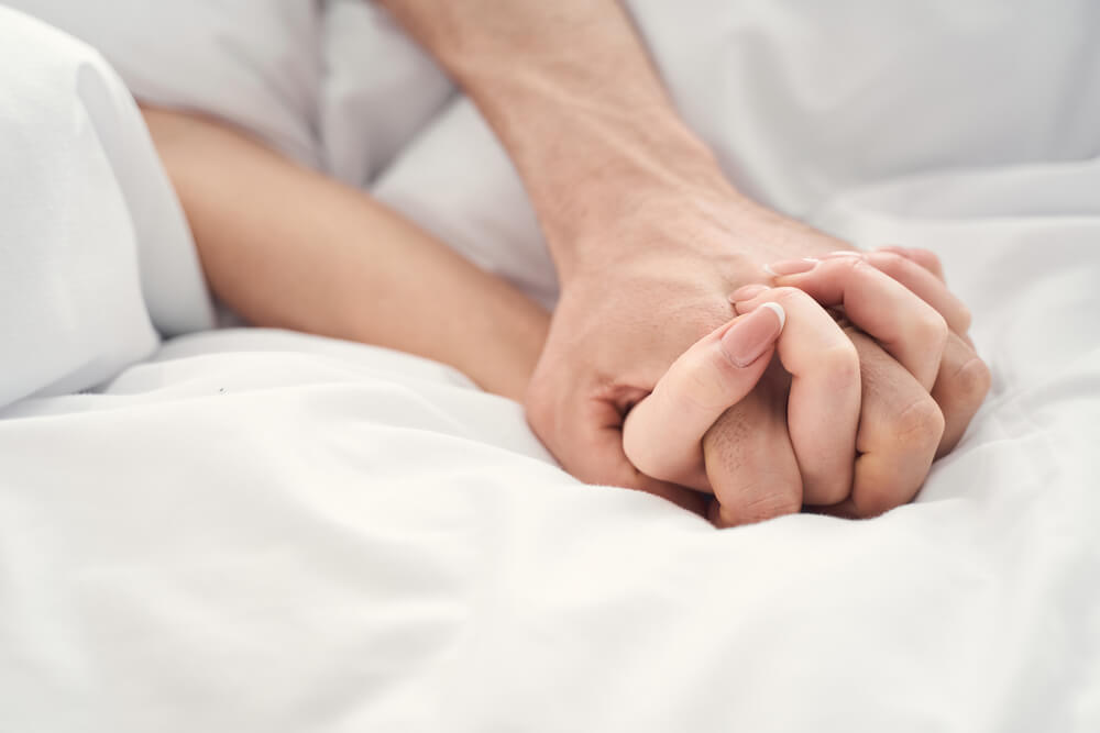 Close Up Of A Young Married Couple Holding Hands During The Moment Of Intimacy In Bed