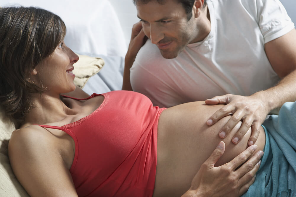 Man Touching Stomach Of Pregnant Woman In Bed At Home