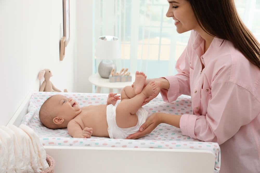 Mother Changing Her Babys Diaper on Table at Home