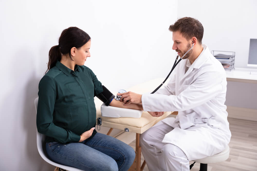 Young Male Doctor Checking Blood Pressure Of Smiling Female Patient In Clinic